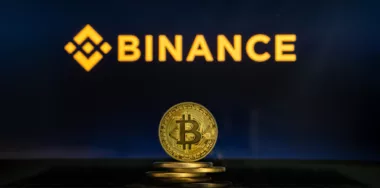 Binance logo on a computer screen with a stack of Bitcoin cryptocurency coins