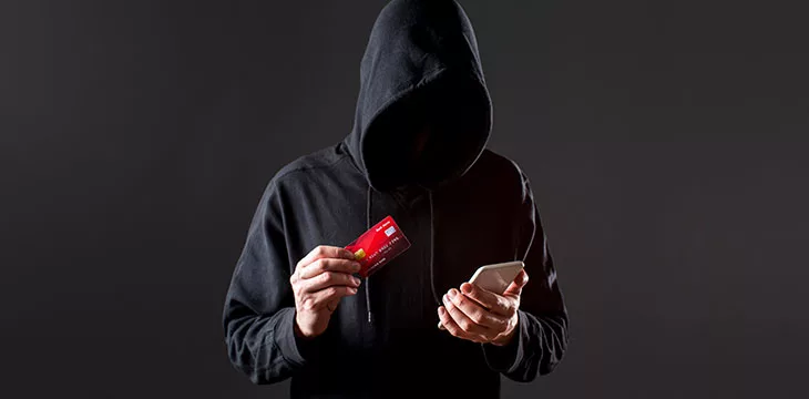 scammer concept hooded person holding a credit card and smartphone