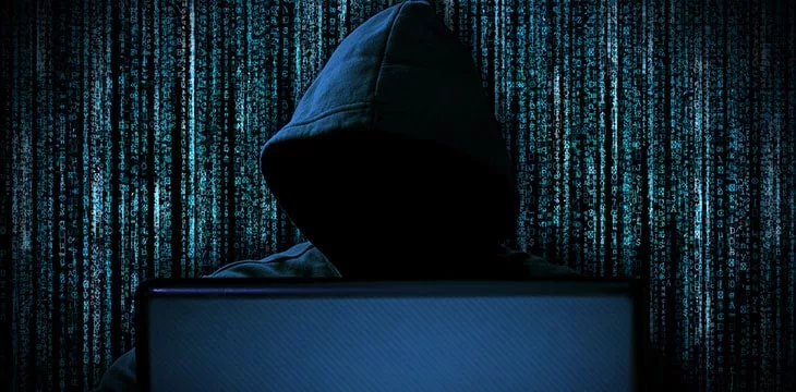 Hacker with red glowing mask behind notebook laptop with Binary background
