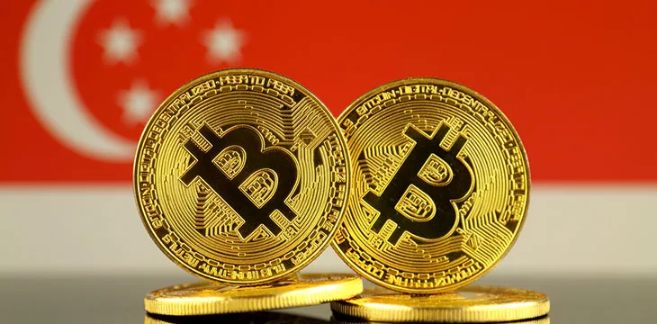 two physical version of Bitcoins on top of two more coins and Singapore Flag in the background
