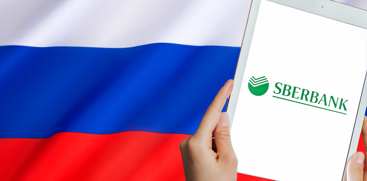 Sberbank on tablet screen being held up with Russian flag in background