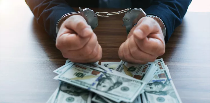 Men in handcuffs with dollar bills on the table