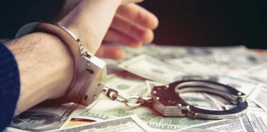 Scammer concept. Handcuffs on hand with US dollar bills underneath