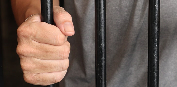 Zoomed photo of a hand holding the gate of his jail cell