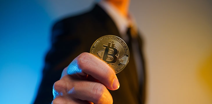 Close up shot of Businessman in black suit holding golden coin isolated on background.