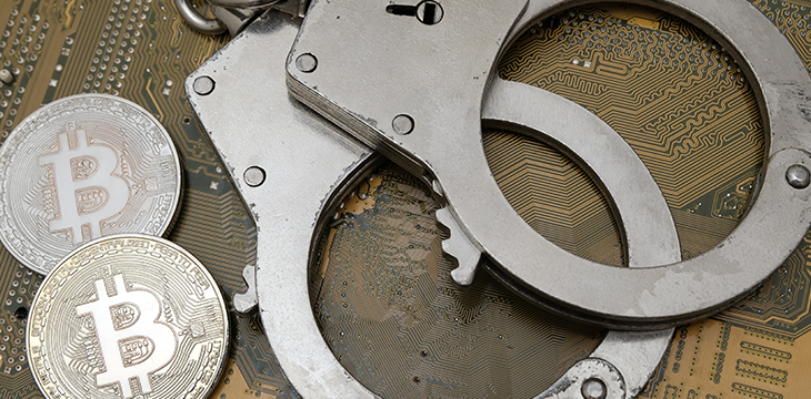 Two coins of bitcoin and handcuffs lie on the background of an electronic printed circuit board.