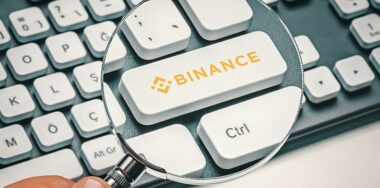 Cryptocurrency trading concept: Male hand holding magnifying glass and focusing computer key with binance coin logo.