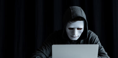 Anonymous internet troll in mask typing on laptop