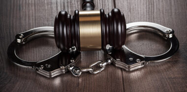 Handcuffs and judge gavel on brown wooden table