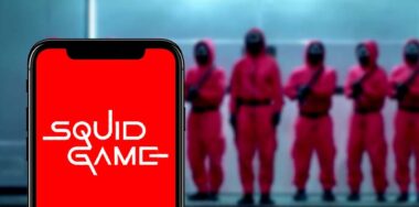 a phone with Squid Game on its screen and Squid Game guards standing behind it