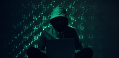 Silhouette of hacker in hoodie using laptop