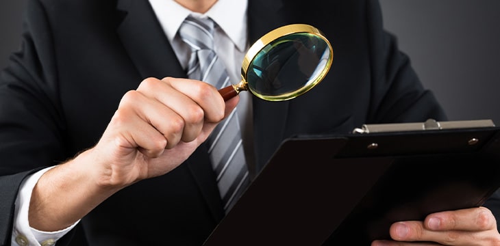 business person inspecting document with magnifying glass