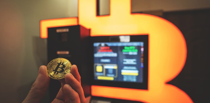 a hand holding a bitcoin in front of a screen