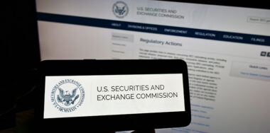 Person holding cellphone with logo of American agency Securities and Exchange Commission (SEC) on screen in front of webpage.