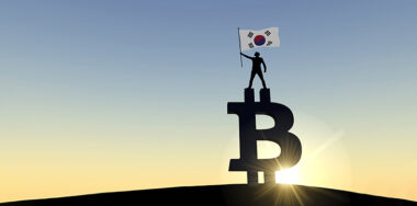 Person waving a south korea flag standing on top of a bitcoin cryptocurrency symbol.