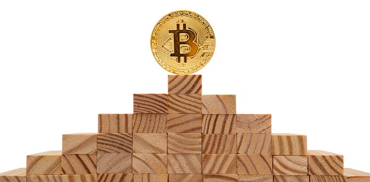 Bitcoin standing on top of a pyramid of wooden cubes.