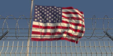Defocused waving flag of the United States behind barbed wire fence.