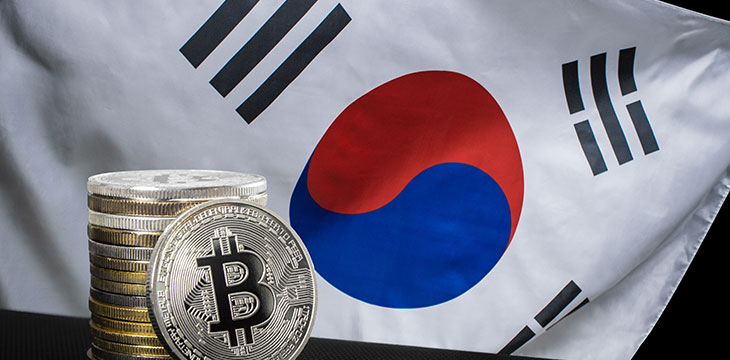 One silver bitcoin and stack of bitcoins over flag of korea