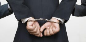 Businessman With Handcuffs While Partners Holding His Arms.