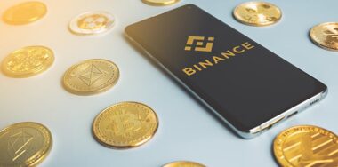 Binance logo on a phone among crypto coins