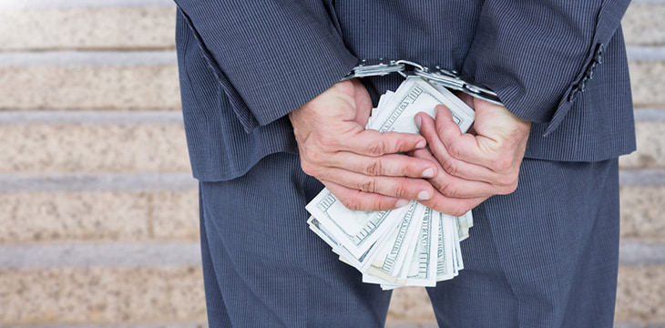 Businessman hands in handcuffs holding US dollar bills