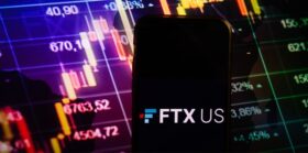 Smartphone displaying logo of FTX US cryptocurrency exchange on stock exchange diagram background