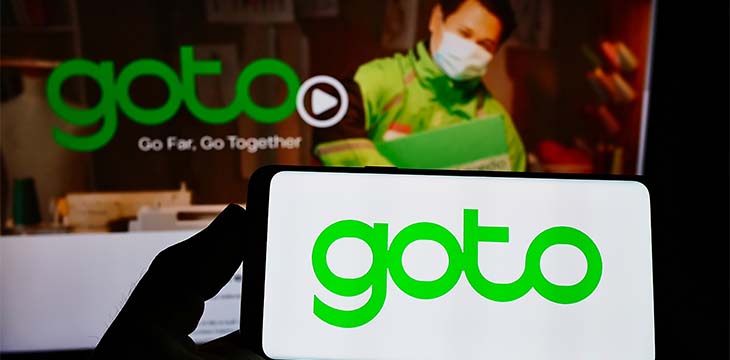 Person holding smartphone with logo of Indonesian company GoTo Group on screen in front of website. Focus on phone display.