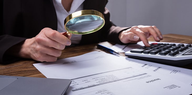 Businessperson's Hand Analyzing Invoice Through Magnifying Glass