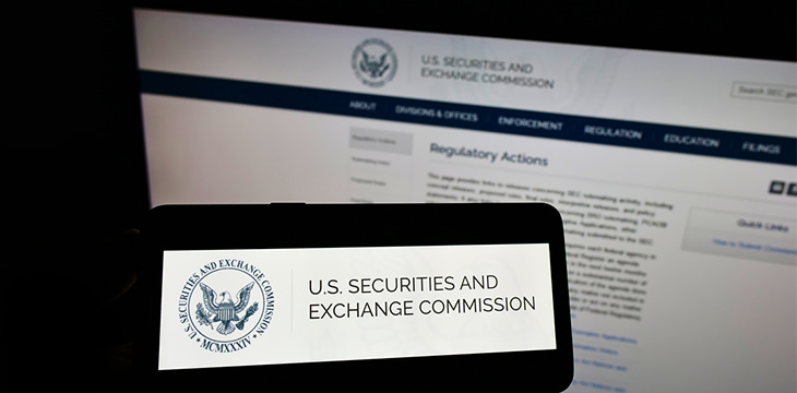 Person holding cellphone with logo of American agency Securities and Exchange Commission (SEC) on screen in front of webpage