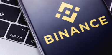 Binance logo on the screen smartphone in front of laptop