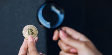 Close up of female hand holding magnifying glass and looking through it at bitcoin