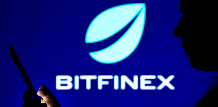 a woman's silhouette holds a smartphone with the Bitfinex logo in the background