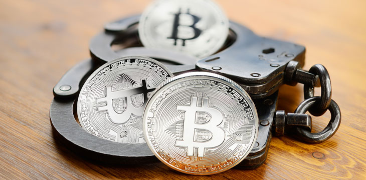 Silver Bitcoin coins and handcuffs on wooden table