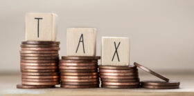 Wooden cubes with the word Tax on stack of coins climbing