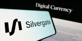 Hand holding the smartphone in front of the PC screen with the symbol of Silvergate