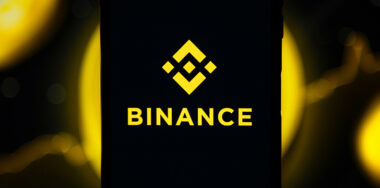 Binance mobile app running at smartphone screen with Binance logo at background