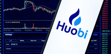 Huobi logo in phone with stocks at the back