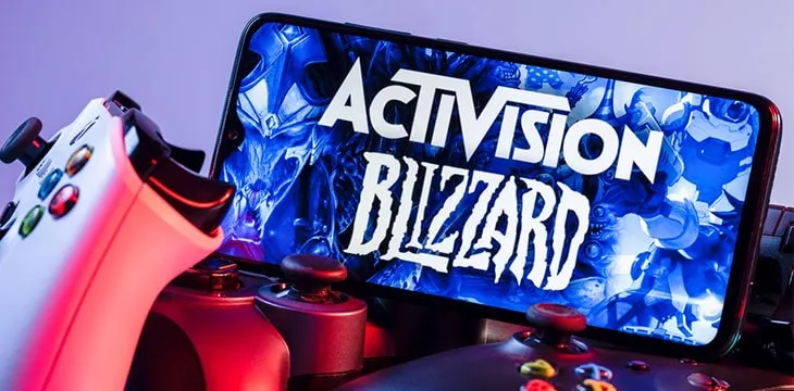 A smartphone with the Activision Blizzard logo on the screen on the pile of the gamepads