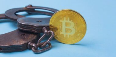 A single gold Bitcoin and handcuffs