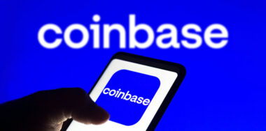 In this photo illustration the Coinbase logo seen displayed on a smartphone and on the background