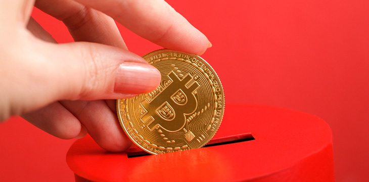 Female hand puts gold coin with bitcoin symbol into slot of red donation box Concept of donorship