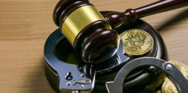 Gavel and handcuffs with bitcoins on a wooden table