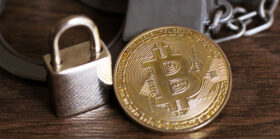 Gold bitcoin, metal lock and handcuffs on a wooden table