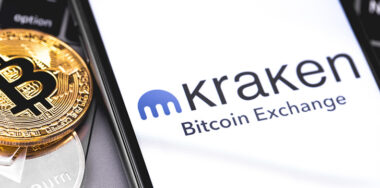 Kraken logo of exchange displayed on the screen of a smartphone with Bitcoin and Ethereum coin on the side
