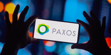 Paxos Trust Company logo seen displayed on a smartphone being held with bokeh background