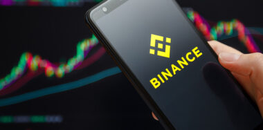 Binance mobile app running at smartphone screen with trading candlestick chart in background