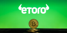 Bitcoin on a stack of coins with eToro logo on a laptop screen. Cryptocurrency and blockchain adoption getting mainstream