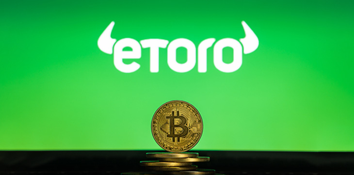 Bitcoin on a stack of coins with eToro logo on a laptop screen. Cryptocurrency and blockchain adoption getting mainstream