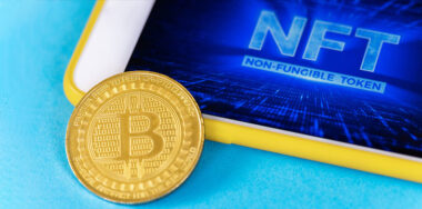 Physical Bitcoin gold coin and smartphone with NFT in it, blue background