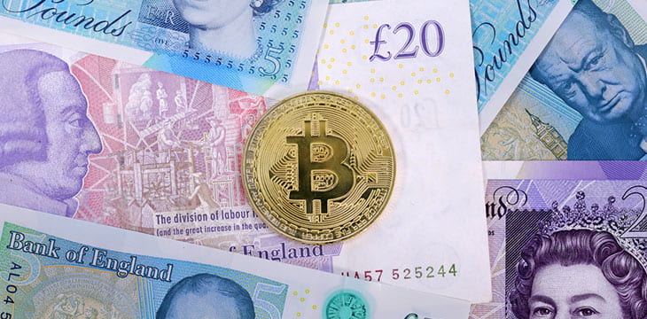 Single virtual cryptocurrency money Bitcoin golden coin on United Kingdom Pound sterling banknotes with faces of Queen Elizabeth II and Winston Churchill